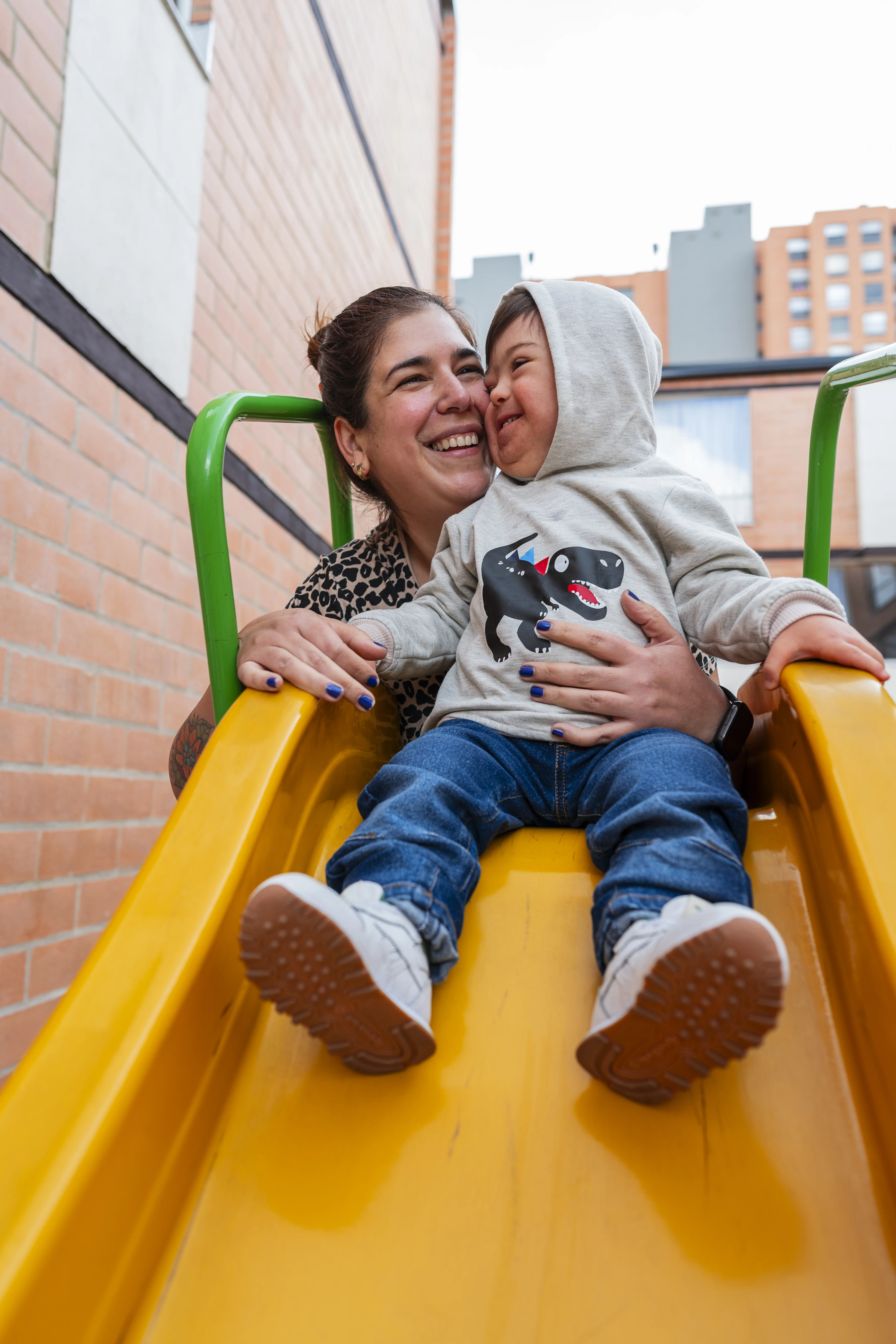 Latino boy with Down syndrome, accompanied by his mother, is in the park playing outdoors while enjoying the moment