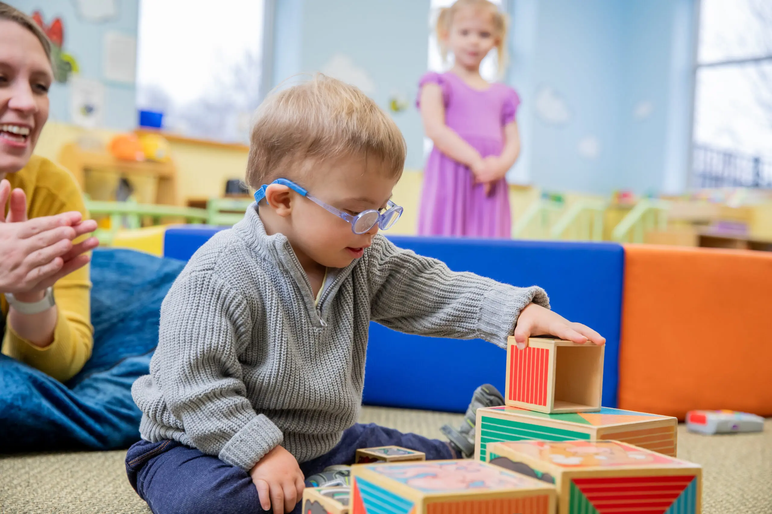 Toddler boy who has Down Syndrome is stacking blocks during appointment with occupational therapist