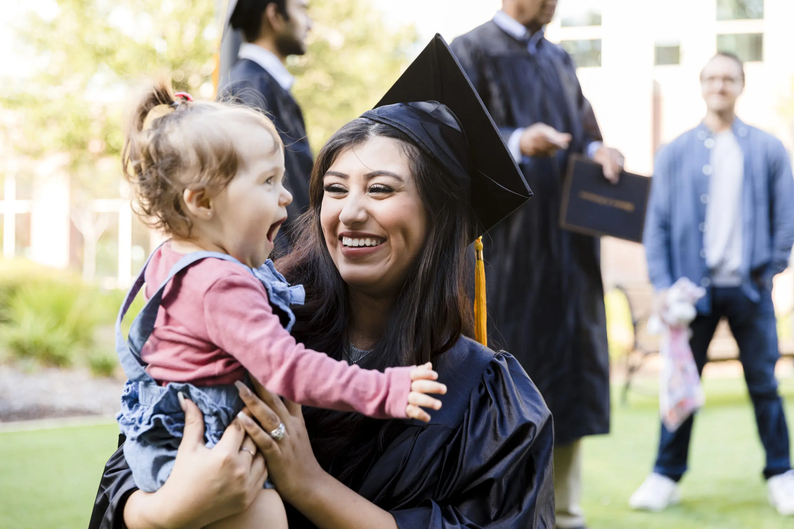 Mother in cap and gown smiles at cute baby daughter Healthy Families America