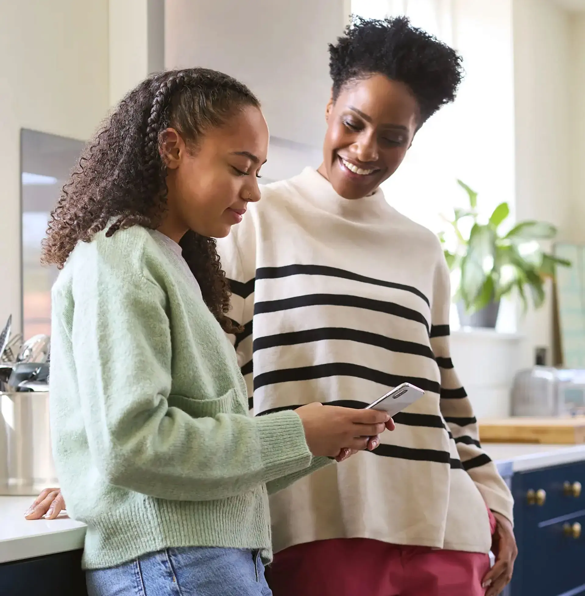 Mother Talking With Teenage Daughter At Home As She Checks Social Media On Mobile Phone